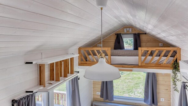 Ett sovrum på entresolplan med ett sluttande tak, en hängande lampa, en inbyggd bänk och ett fönster med gardiner.