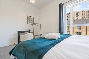 Ein Hotelzimmer mit Bett, Heizkörper, einem Vorhangfenster, einem gerahmten Bild an der Wand und Blick auf ein Gebäude.