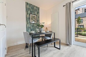 En matplats med ett bord dukat för två personer, en bänk och utsikt över en byggnad genom ett fönster.