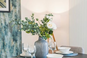 Ein Esstisch mit Blumen in einer Vase, zwei Weingläsern und einer Schüssel.