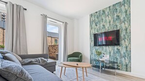 Ein modernes Wohnzimmer mit einem grauen Sofa, einem grünen Sessel, einem Holztisch und einem an einer strukturierten Wand befestigten Fernseher.