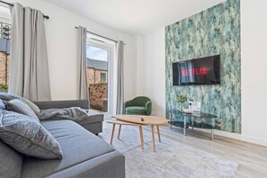 Ein modernes Wohnzimmer mit einem grauen Sofa, einem grünen Sessel, einem Holztisch und einem an einer strukturierten Wand befestigten Fernseher.