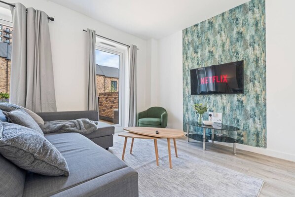 Ett modernt vardagsrum med en grå soffa, en grön fåtölj, ett träbord och en tv som är monterad på en vägg med en intressant yta.