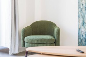 Une pièce avec un fauteuil à revêtement vert, une table en bois et un mur blanc.