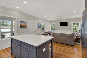 Una cocina moderna con una isla grande, comedor con sillas, un sofá y un televisor de pantalla plana montado en la pared.