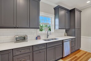 Una cocina moderna con gabinetes grises, una encimera blanca, un tostador integrado y una ventana con vista a zonas verdes.