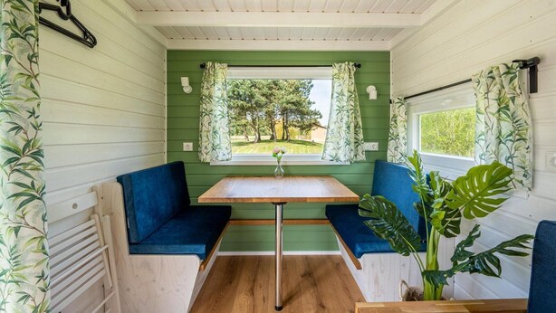 Un intérieur chaleureux avec une table en bois et deux sièges bleus rembourrés, une fenêtre donnant sur un paysage verdoyant et un radiateur blanc.