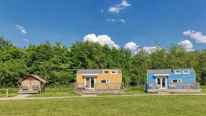 Trois cabanes, avec un champ herbeux et des arbres en arrière-plan.