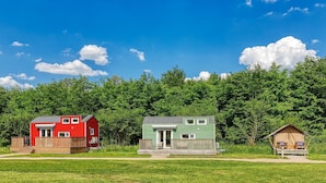 Une cabane rouge et verte avec une terrasse, entourée d’une forêt.