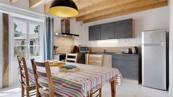 A modern kitchen with wooden beams, a dining table with striped tablecloth, and a large window.