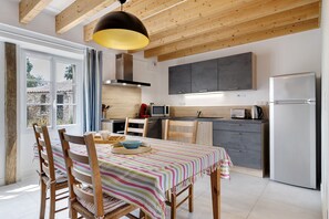 A modern kitchen with wooden beams, a dining table with striped tablecloth, and a large window.