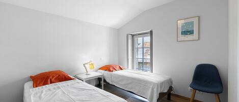 A room with two beds, a desk, a chair, a window, and a hanging light fixture.