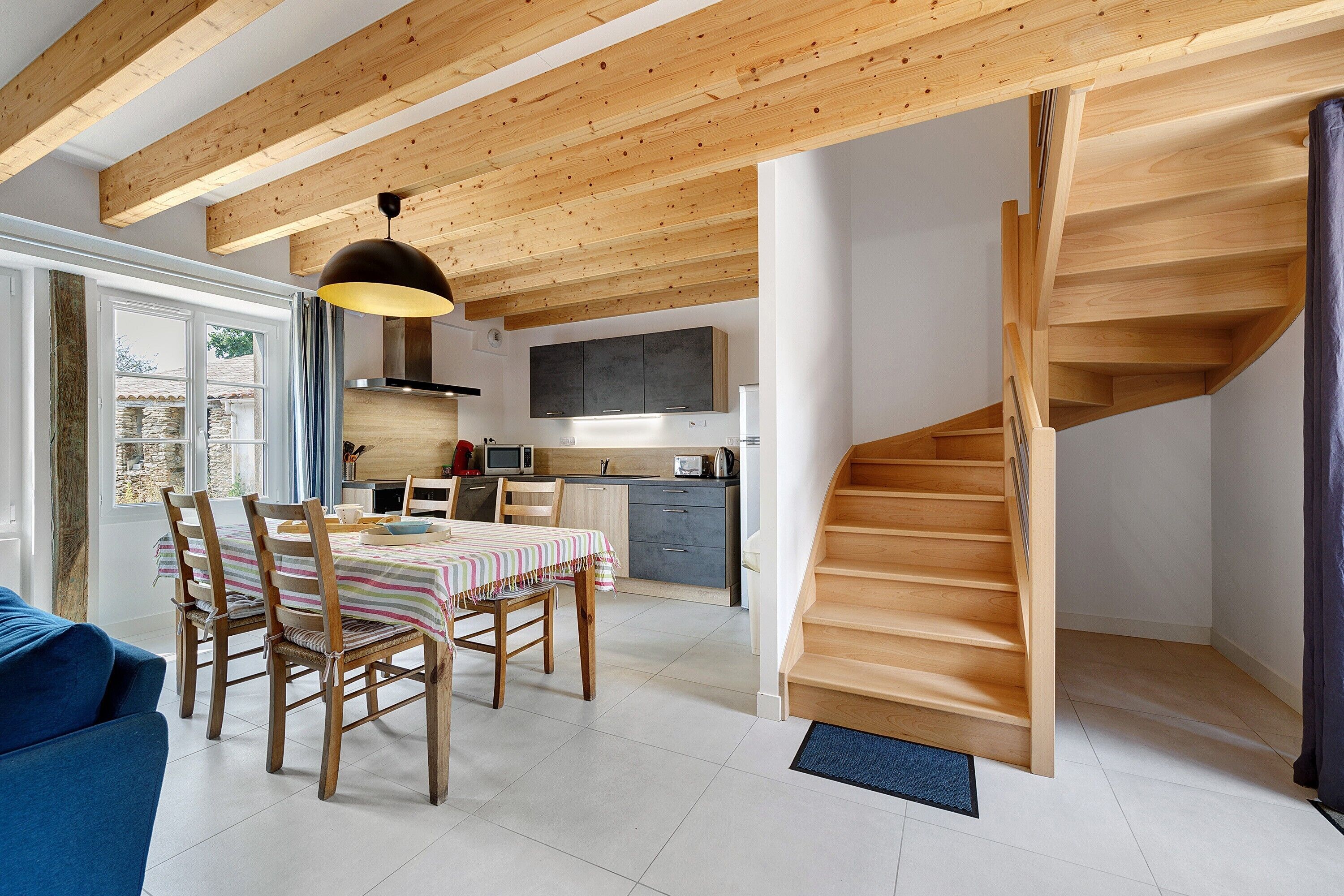 A modern kitchen with wooden beams, a dining area with a striped tablecloth, and a wooden staircase.