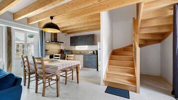 A modern kitchen with wooden beams, a dining area with a striped tablecloth, and a wooden staircase.
