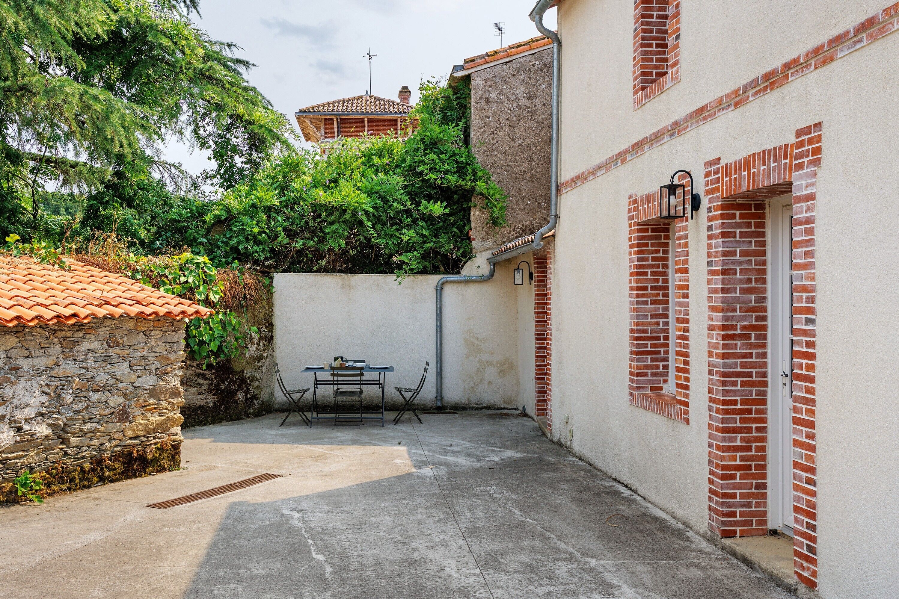 A courtyard with a stone wall, a table with chairs, and a building with red brick and white walls.