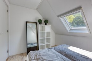 Et soveværelse med ovenlys, et stort spejl og en hvid garderobe.