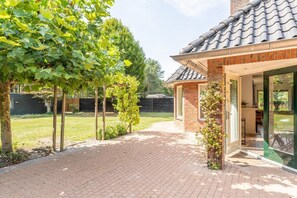 Een huis van baksteen met een pannendak, een geplaveid pad en een tuin met bomen.