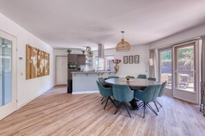 A modern kitchen with a central island, a dining area with a round table and chairs, and a large window providing a view of the outdoors. - De Glamping - Villa with sleeping lodge & wellness facilities (Zeewolde)