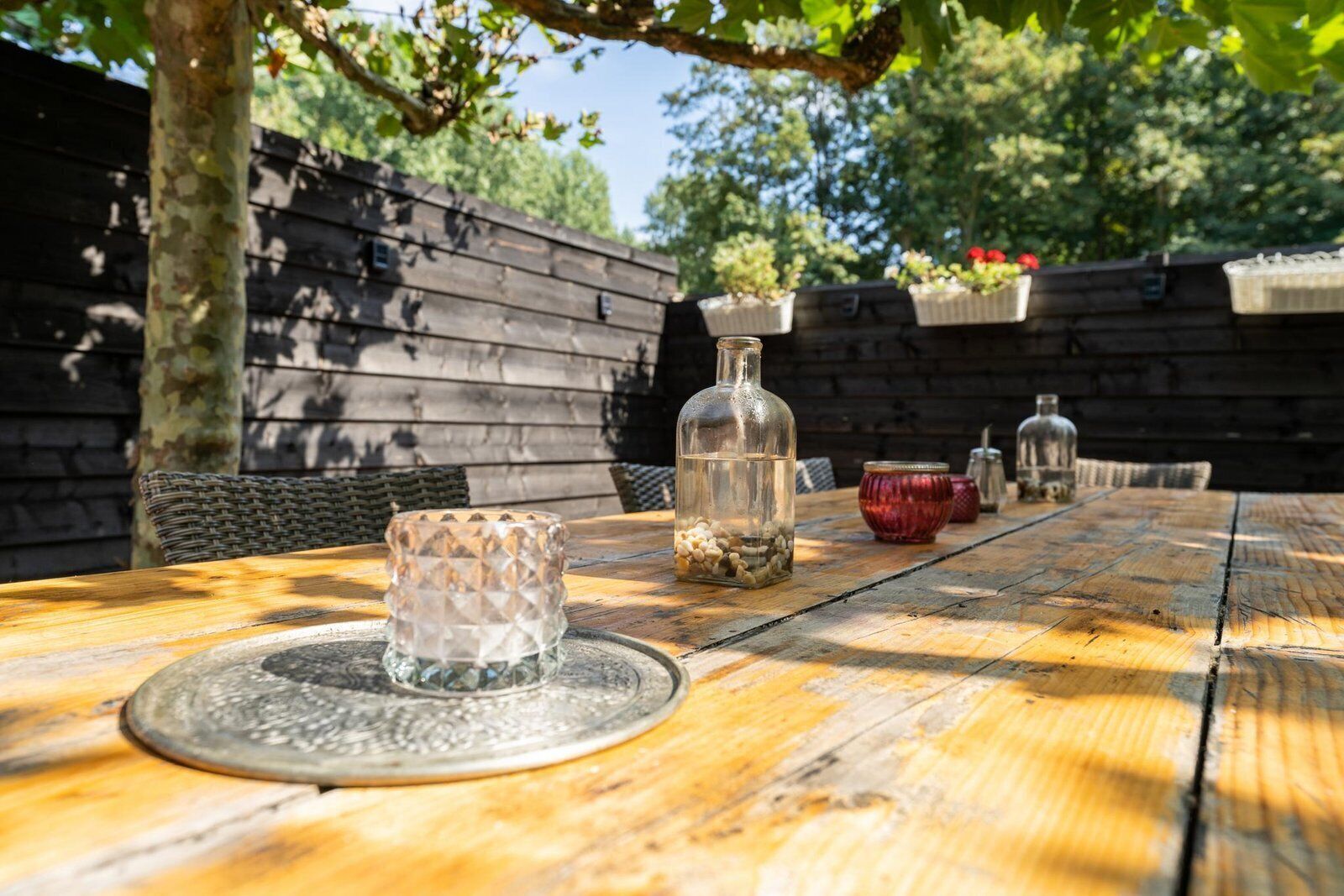 Ein Holztisch mit einer Glasflasche und einem Glasbehälter mit weißen Steinen, umgeben von Korbstühlen.