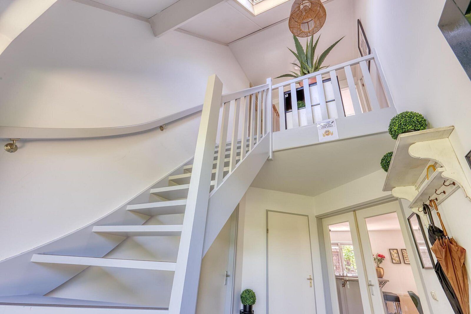 Un escalier blanc menant à un palier du deuxième étage, agrémenté d’une balustrade blanche, d’un luminaire suspendu et d’une plante en pot.