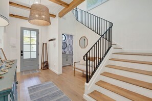 Eine Treppe mit Holzdielen und schwarzen Geländern, einer gewebten Leuchte, einer Tür mit Fenster sowie einer Wand mit rundem Spiegel und Wanddekoration.