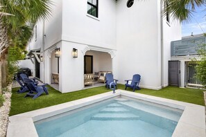 A residential pool area with a clear blue pool, surrounded by a white house with a covered patio, and blue Adirondack chairs. - Sail Away Estate: 5BDR with Private Pool (Tybee Island)