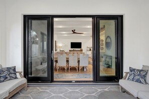 Un salon moderne avec un canapé, un coin repas comprenant une table et des chaises, et une porte-fenêtre coulissante donnant sur la cuisine.