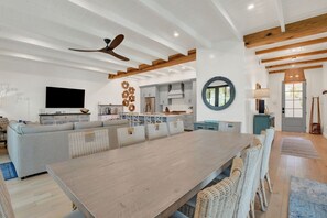 Un vaste espace de vie comprenant une grande table à manger en bois, un canapé et une cuisine à l’arrière-plan.