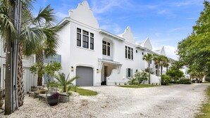 A white colonial-style building with a gravel driveway and palm trees. - Sail Away Estate: 5BDR with Private Pool (Tybee Island)