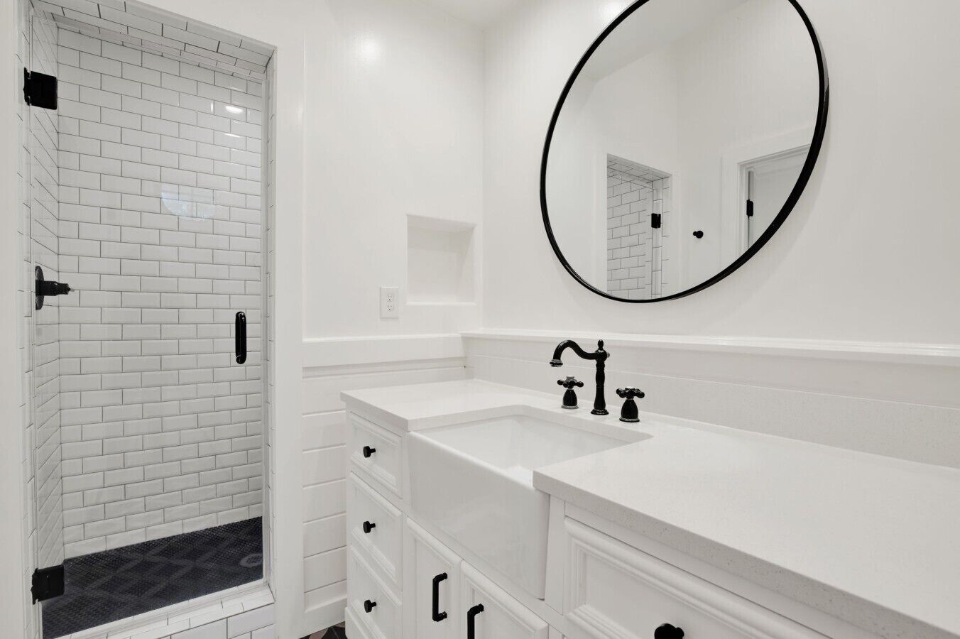 A modern bathroom with a white tiled shower, a large mirror, and a double sink with black faucets.