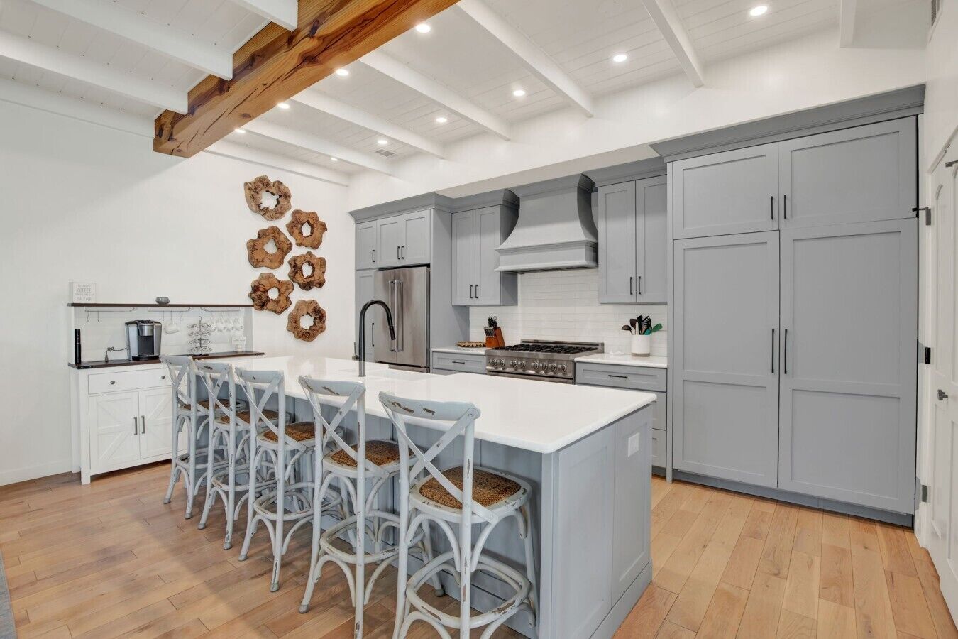 A modern kitchen with a central island, grey cabinets, and a wooden ceiling beam.