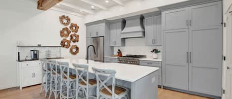 A modern kitchen with a central island, grey cabinets, and a wooden ceiling beam.