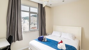A hotel room with a bed, a desk, a chair, a window with curtains, and a ceiling fan. - Edifício Rio Parnaíba (Rio de Janeiro)
