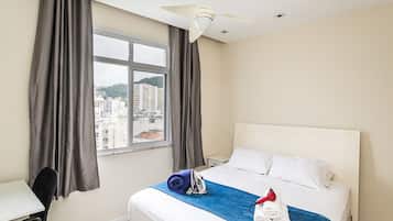 Quarto de hotel com cama, escrivaninha, cadeira, janela com cortinas e ventilador de teto.