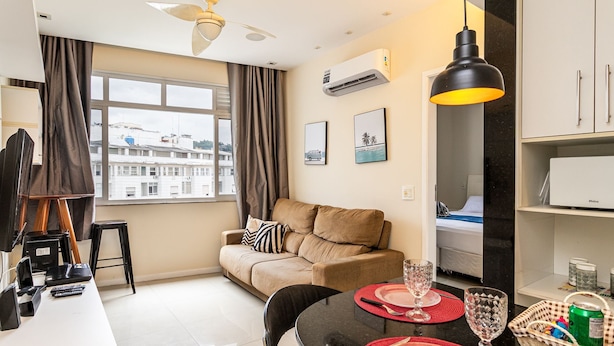 A modern living room with a sofa, dining table, and a view of the cityscape through large windows. - Edifício Rio Parnaíba (Rio de Janeiro)
