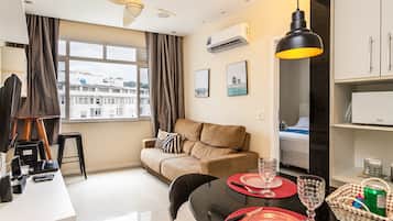Sala de estar moderna com sofá, mesa de jantar e vista para a cidade através de grandes janelas.