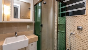 A bathroom with a white sink, a glass-enclosed shower, and a tiled wall. - Edifício Rio Parnaíba (Rio de Janeiro)