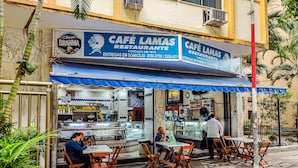 A café with outdoor seating, a blue awning, and a sign indicating it is a restaurant. - Edifício Rio Parnaíba (Rio de Janeiro)