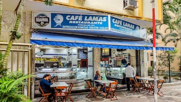 Um café com mesas ao ar livre, toldo azul e placa indicando que é um restaurante.