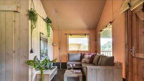 Une pièce chaleureuse avec un banc en bois, un canapé et une petite table. On y trouve des plantes et une fenêtre qui laisse entrer la lumière naturelle.
