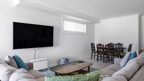 Een woonkamer met een flatscreen televisie, een houten salontafel, een bank en een eethoek met stoelen en een tafel.
