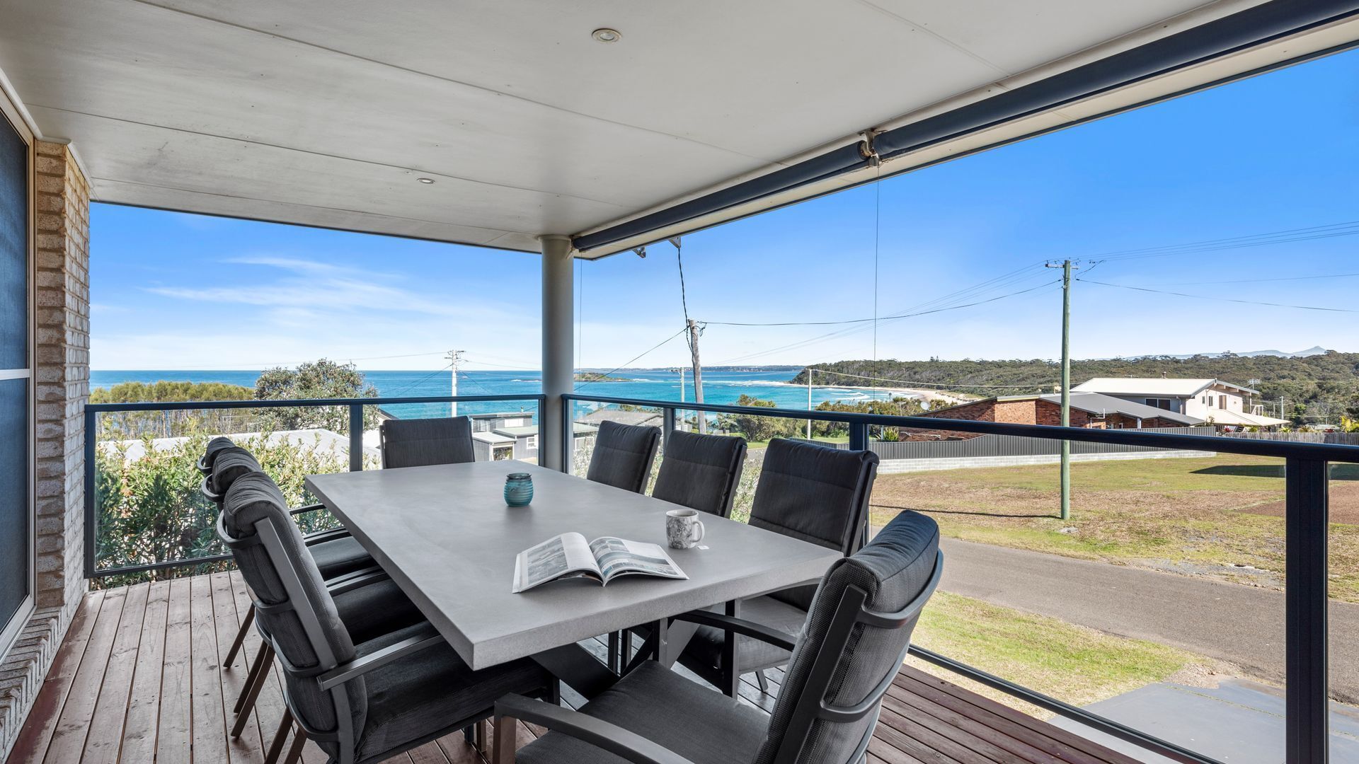 A covered outdoor dining area with a table and chairs, overlooking a coastal landscape.