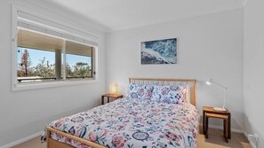 Ein Schlafzimmer mit einem Bett, einem Fenster, einem Wandbild und Nachttischen.