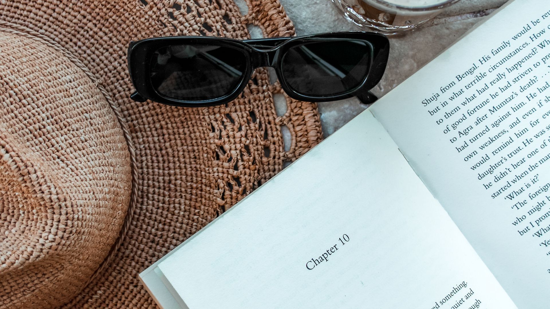 Ein Buch, das auf Kapitel 10 liegt, eine schwarze Sonnenbrille und ein braunes Gewebestück, möglicherweise eine Tasche oder ein Kissen.