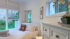 Ein Schlafzimmer mit einem Bett, einem Schminktisch und einem Fenster mit einer Orchideenpflanze.