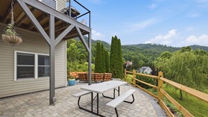 Une terrasse avec une table de pique-nique et des chaises, une plante suspendue et une vue sur une zone boisée.