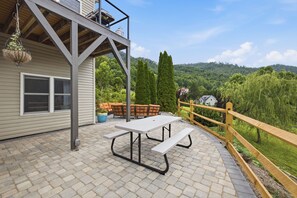 Eine Terrasse mit Picknicktisch und Stühlen, einer hängenden Pflanze und Blick auf ein bewaldetes Gebiet.