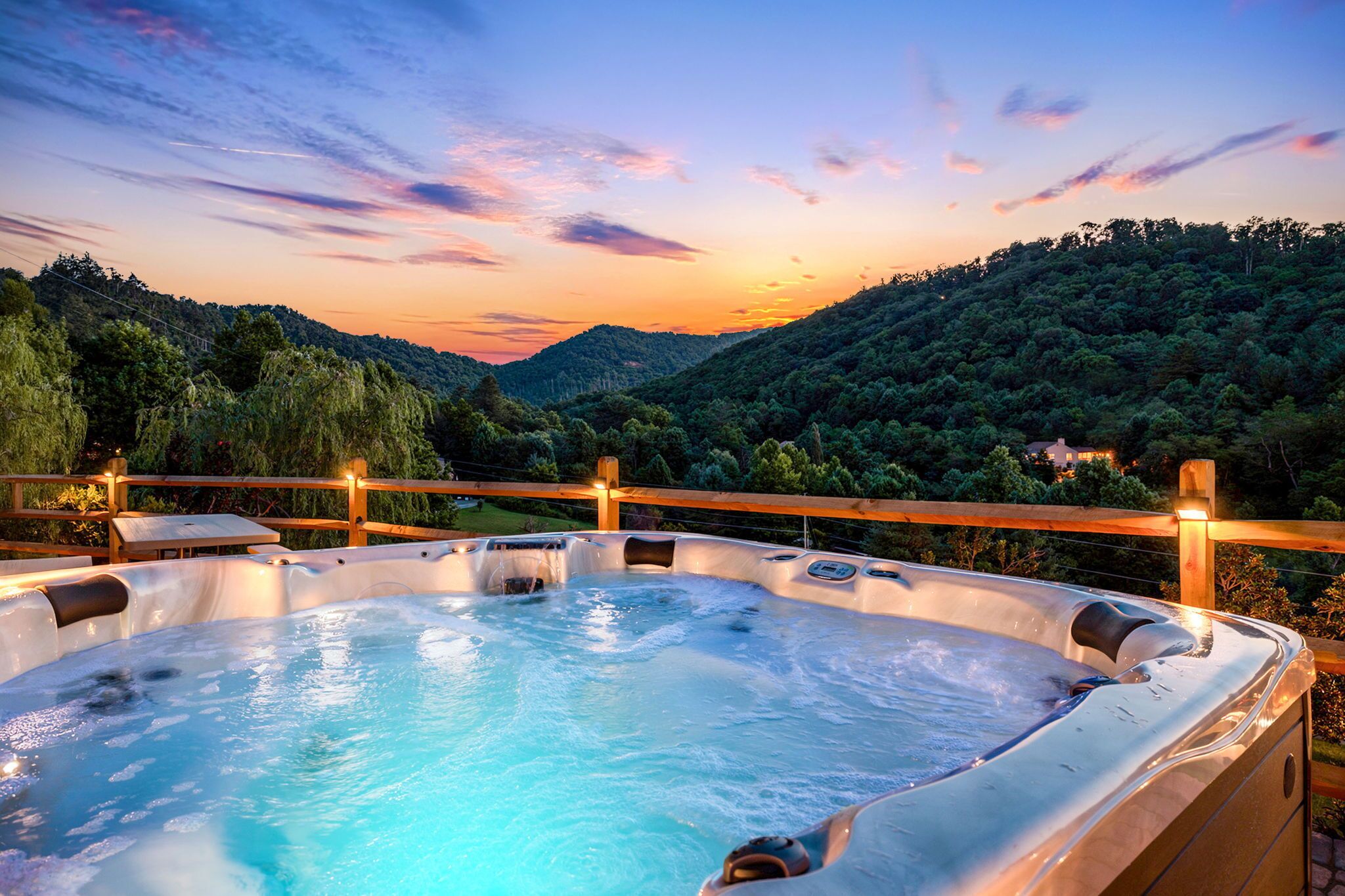 Ein Whirlpool mit Holzterrasse und Geländer, umgeben von einer gebirgigen Landschaft.