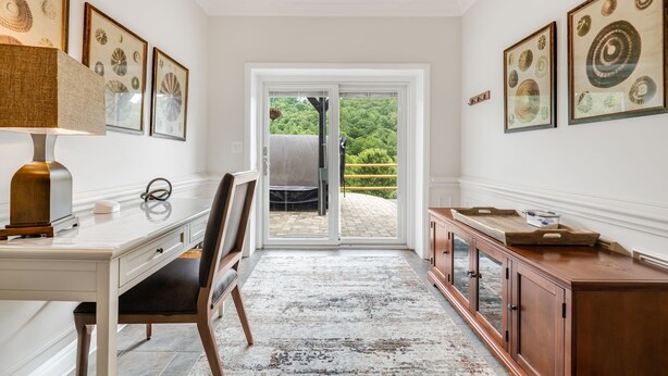 Une pièce avec un bureau blanc, une chaise, une lampe et un meuble. Des tableaux encadrés ornent les murs.