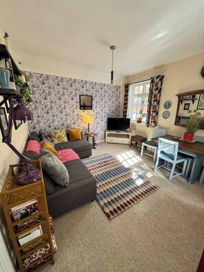 Ein Wohnzimmer mit einer Couch, einem Fernseher, einem Couchtisch und einem Bücherregal.